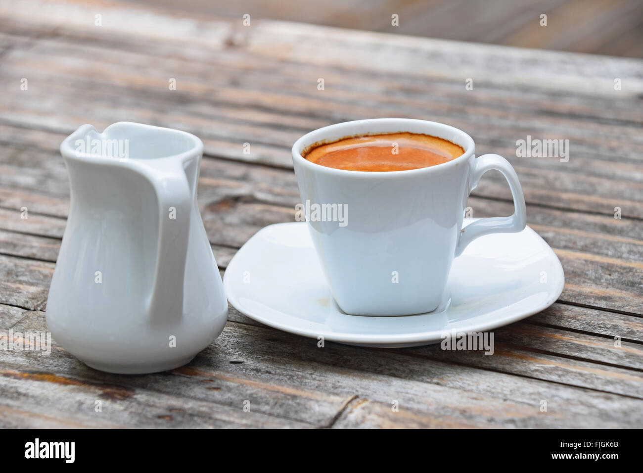 Uno bianco coppa piena di caffè espresso con crema marrone su porcellana  piattino con piccolo bricco per il latte sul vecchio vintage in legno di  bambù tabl Foto stock - Alamy
