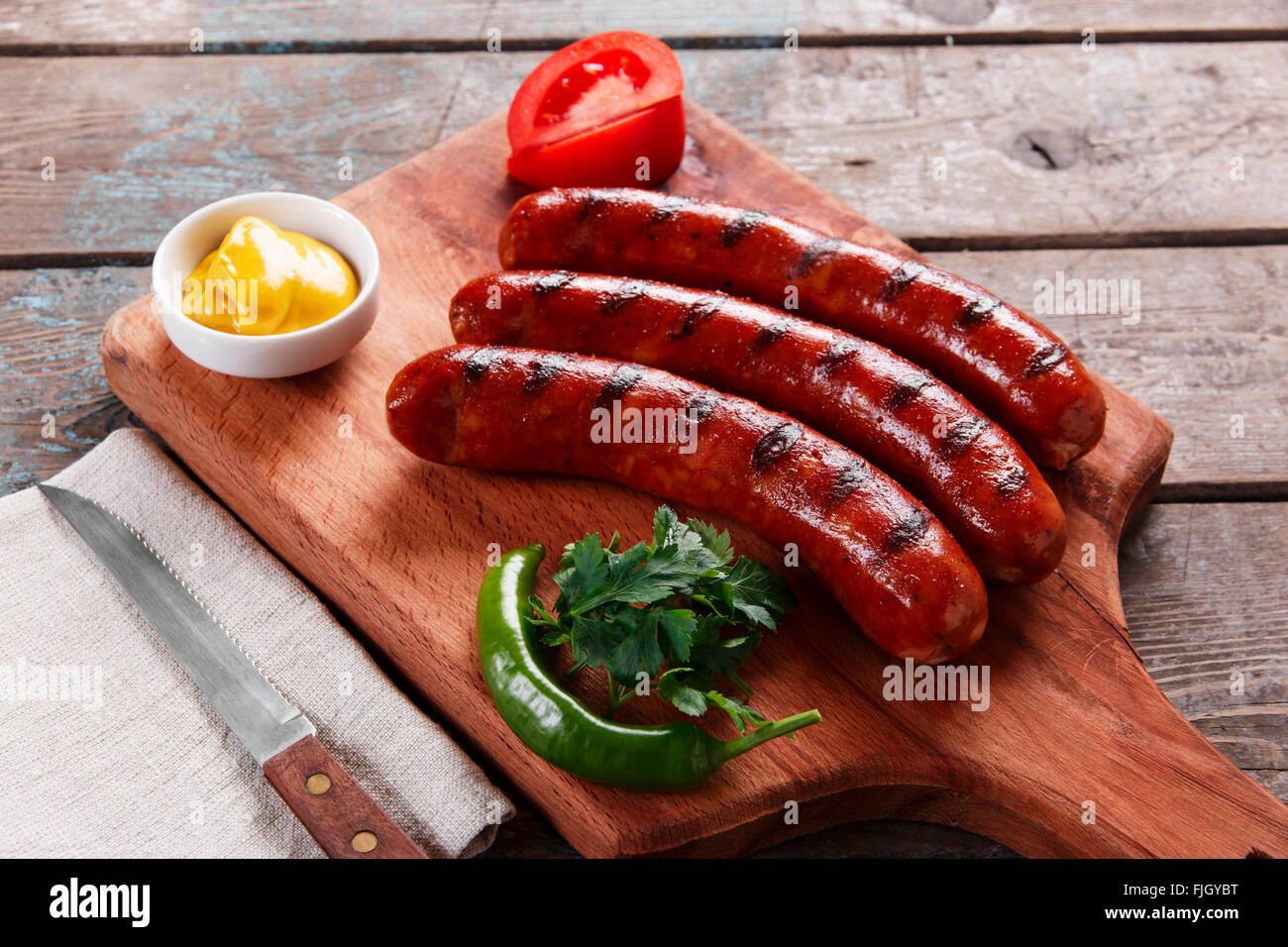 Salsicce alla griglia su una tavola di legno con il sugo di pomodoro e verdure Foto Stock