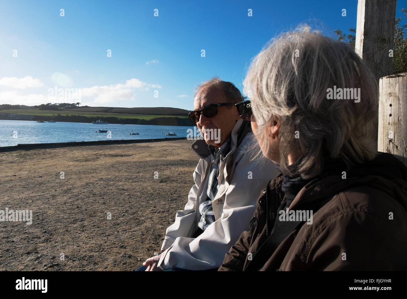 Coppia in pensione seduta su una panchina in riva al mare al Rock, Cornwall, Regno Unito. Foto Stock