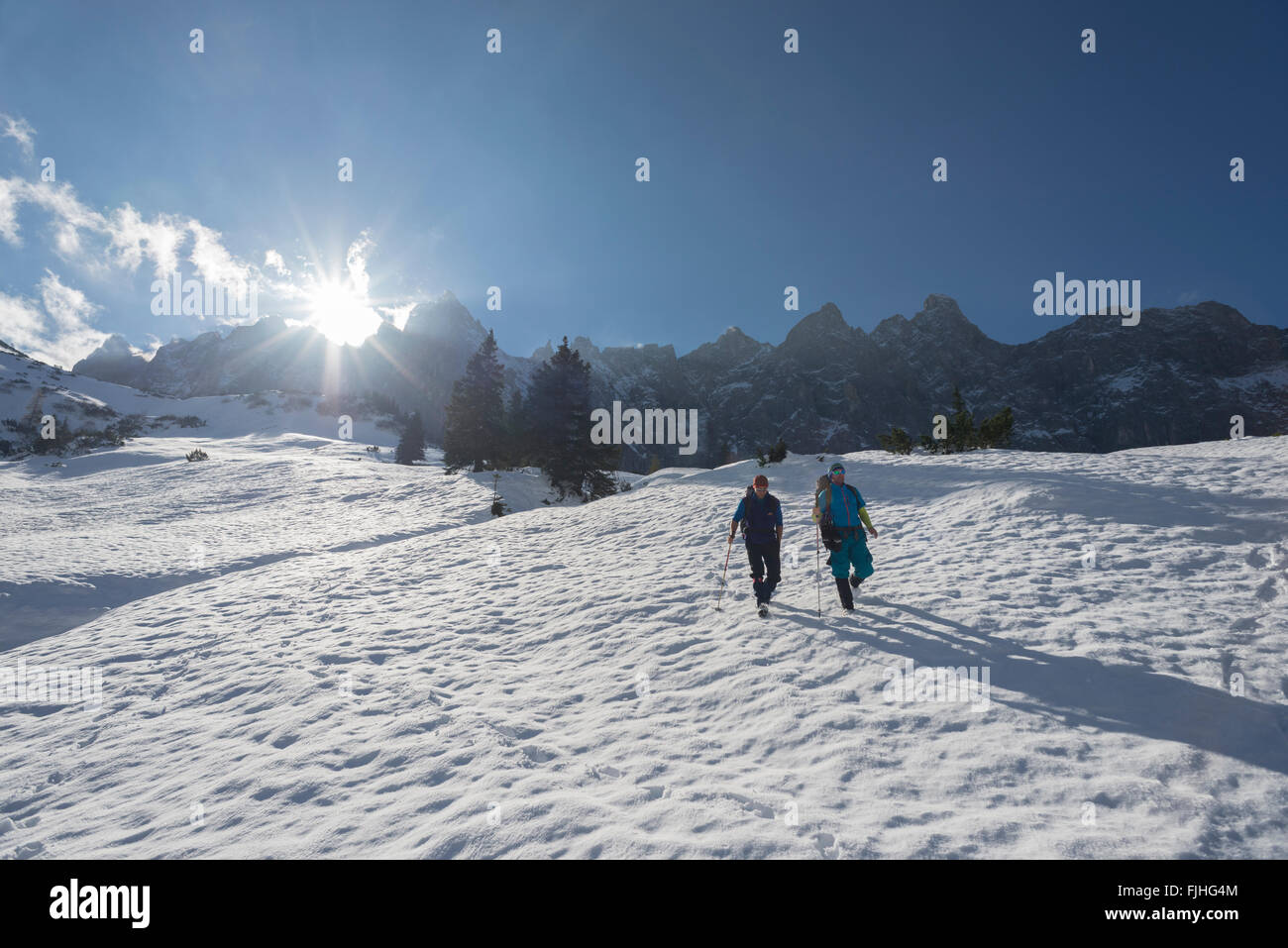 Due escursionisti durante la discesa del Falcon rifugio a Ladiz alp su nevai retroilluminati da sole, Karwendel, Tirolo, Austria Foto Stock