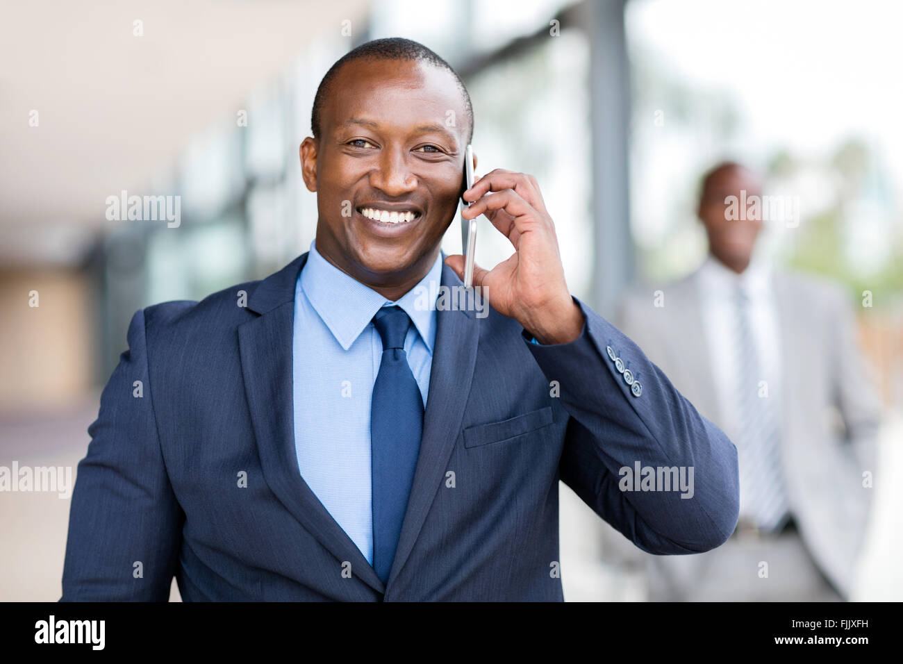 Allegro imprenditore africano parlando al cellulare in ufficio Foto Stock