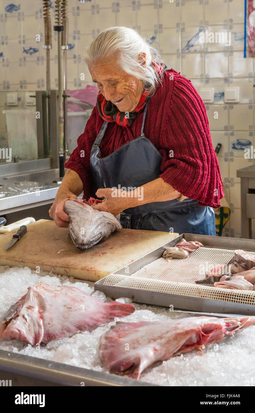 Gentile vecchia donna pescivendolo pulizia di pesce fresco in preparazione per la vendita nel mercato pubblico, Cascais, Portogallo Foto Stock