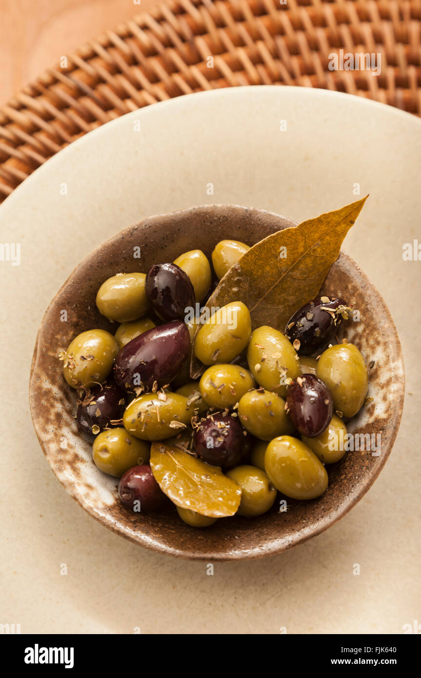 Lo stile mediterraneo antipasto di Francese picholine verde e nero greca di olive kalamata con foglie di alloro e le erbe aromatiche essiccate nel piatto di portata Foto Stock