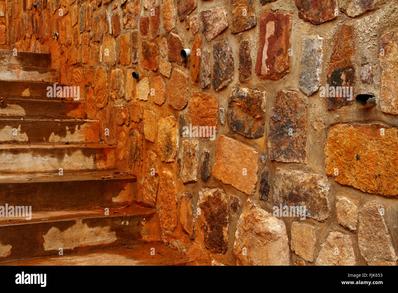 Una parete di roccia con grandi lastre di pietra e tubi di drenaggio spuntano fuori di esso. Scala corre lungo il lato. A Kigali Genocide Mem Foto Stock