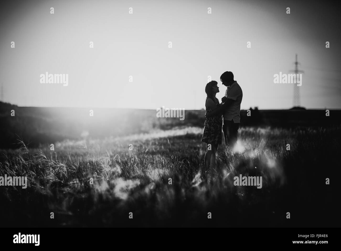 Bianco nero fotografia coppia romantica in piedi e baciare su sfondo prato estivo tramonto Foto Stock