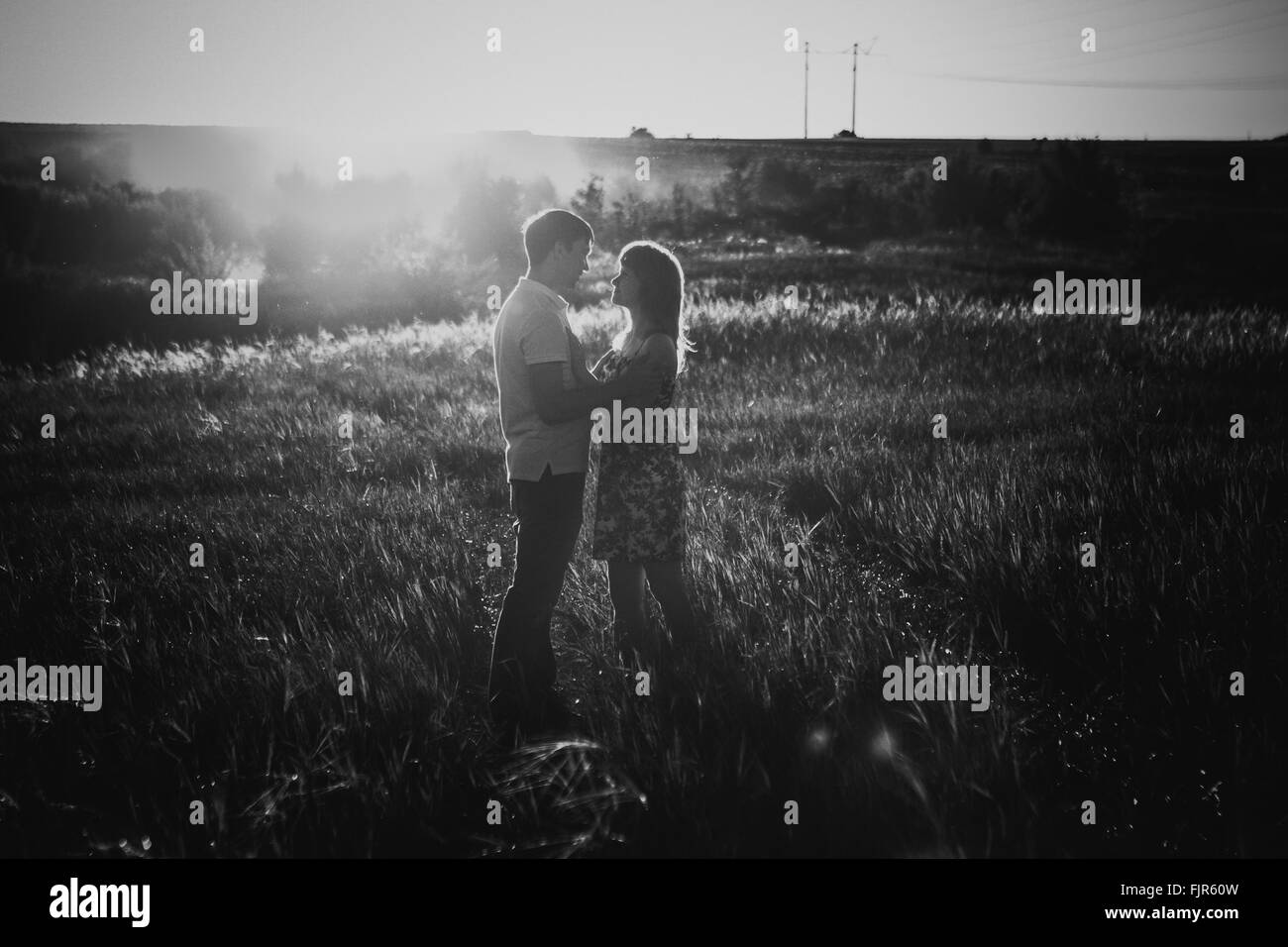 Bianco nero fotografia coppia romantica in piedi e baciare su sfondo prato estivo tramonto Foto Stock