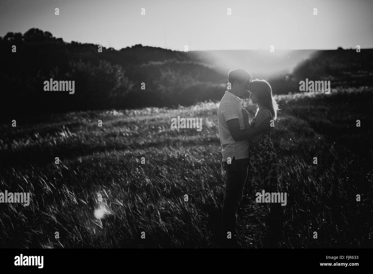 Bianco nero fotografia coppia romantica in piedi e baciare su sfondo prato estivo tramonto Foto Stock