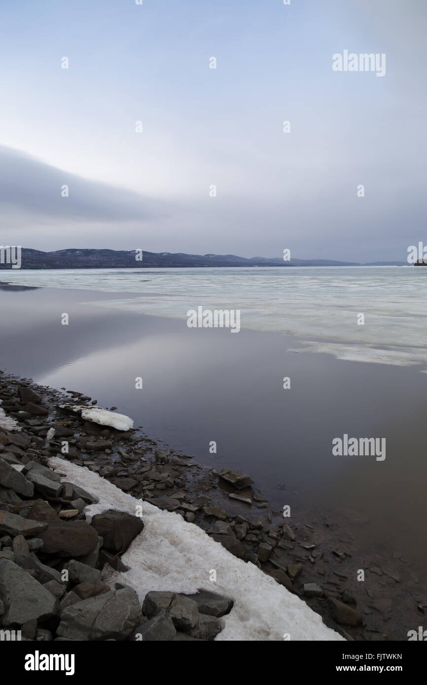 Ghiaccio galleggiante sul St Lawrence River in Gaspe, Quebec. La neve copre metà rocky riverside e il cielo è parzialmente nuvoloso in t Foto Stock