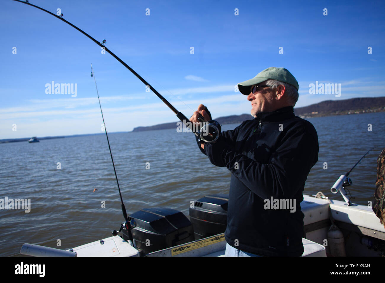 L'uomo la bobinatura nel pesce della parte posteriore di una barca sul fiume Hudson, New York Foto Stock