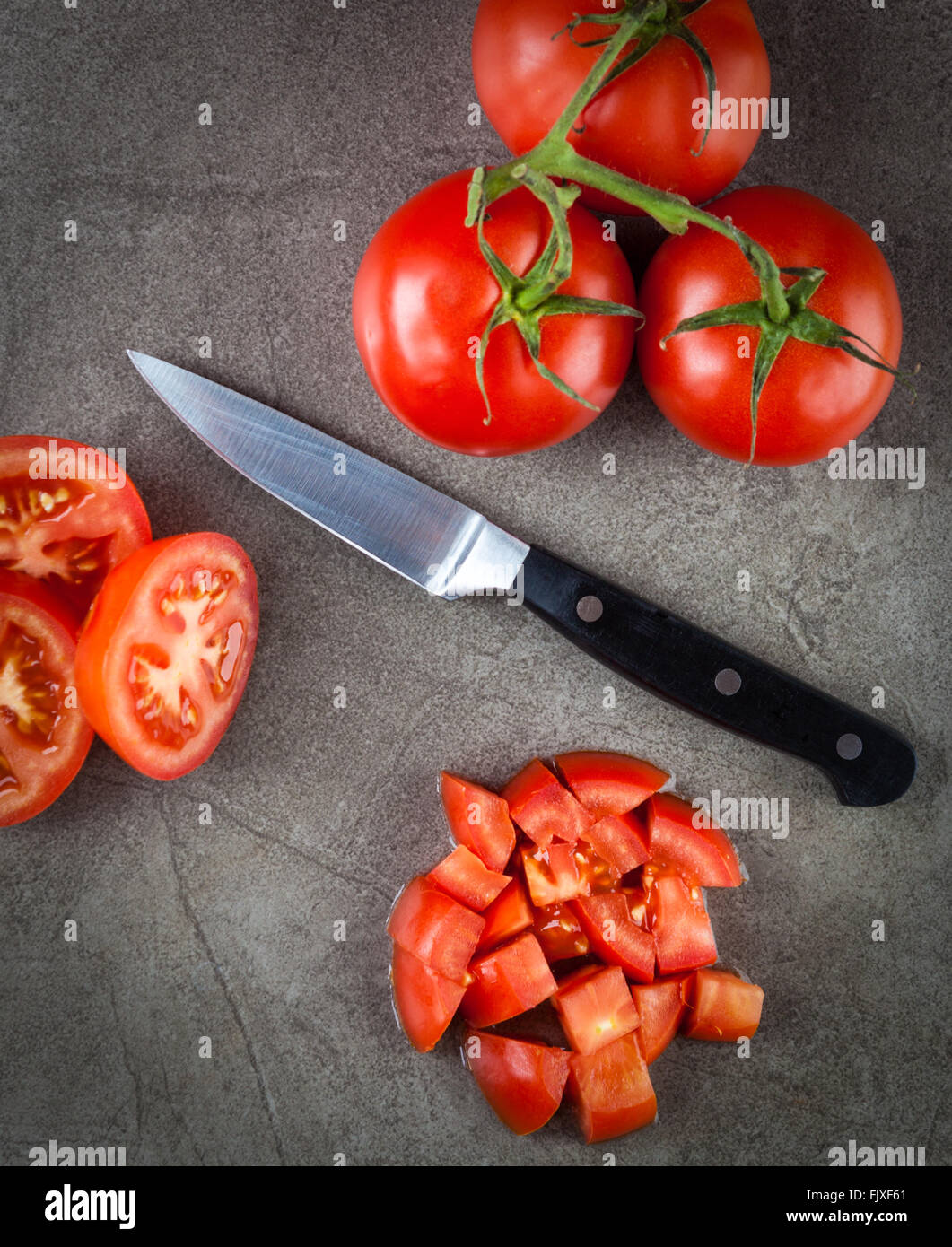 Pomodori di travatura reticolare e coltello da cucina disposti sulla trama della superficie di pietra. Vista dall'alto. Foto Stock