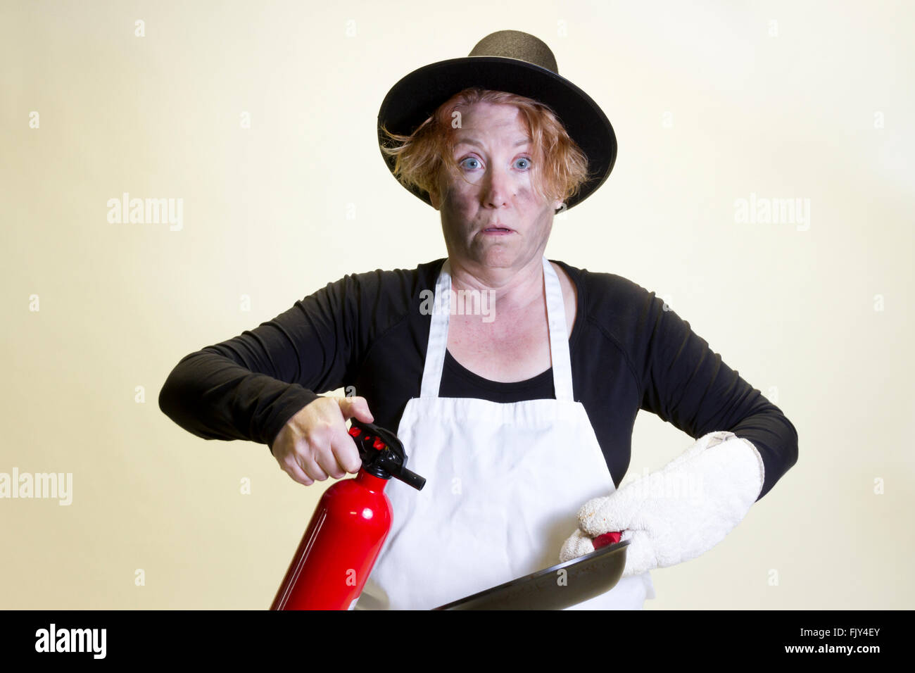 Donna matura con firmato faccia tenendo pan e estintore con pellegrino hat e grembiule. Foto Stock