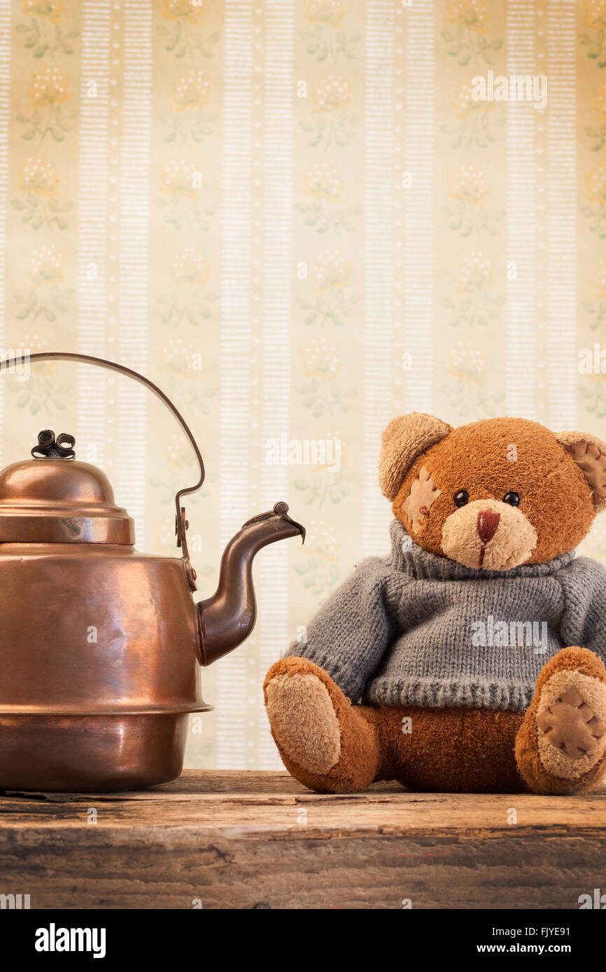 Orsacchiotto di peluche e bollitore in rame sullo sfondo della vecchia carta da parati Foto Stock