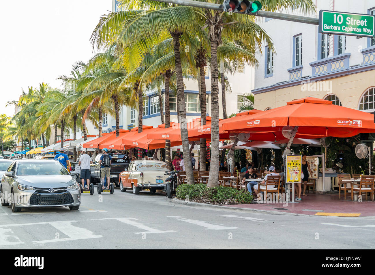 Persone, automobili e terrazze all'aperto sulla Ocean Drive a incrocio 10th Street in South Beach di Miami Beach, Florida, Stati Uniti d'America Foto Stock