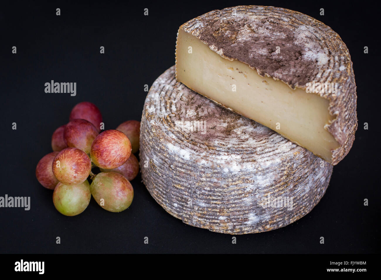 Testa di semi-rigida di età compresa tra i formaggi di capra e Uva su sfondo nero Foto Stock