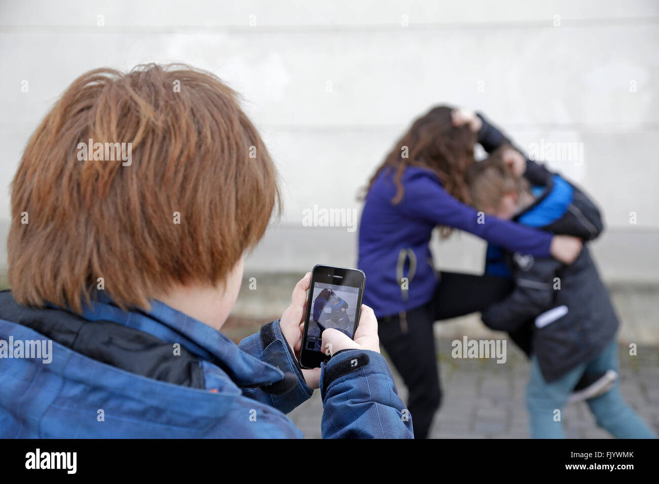 Due bambini combattimenti, terzo uno facendo un video con lo smartphone Foto Stock