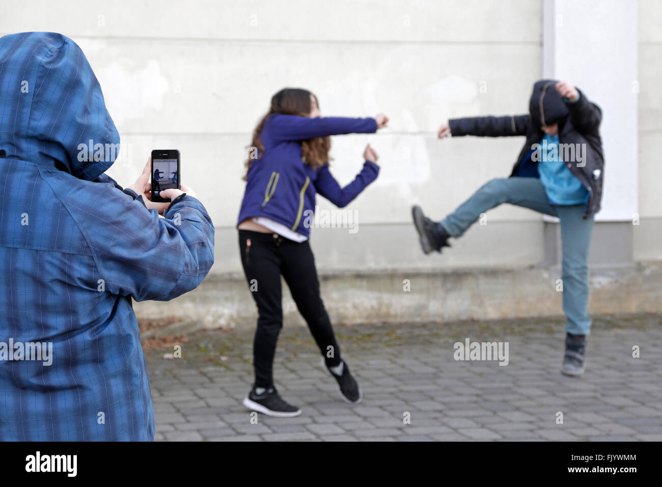 Due bambini combattimenti, terzo uno facendo un video con lo smartphone Foto Stock