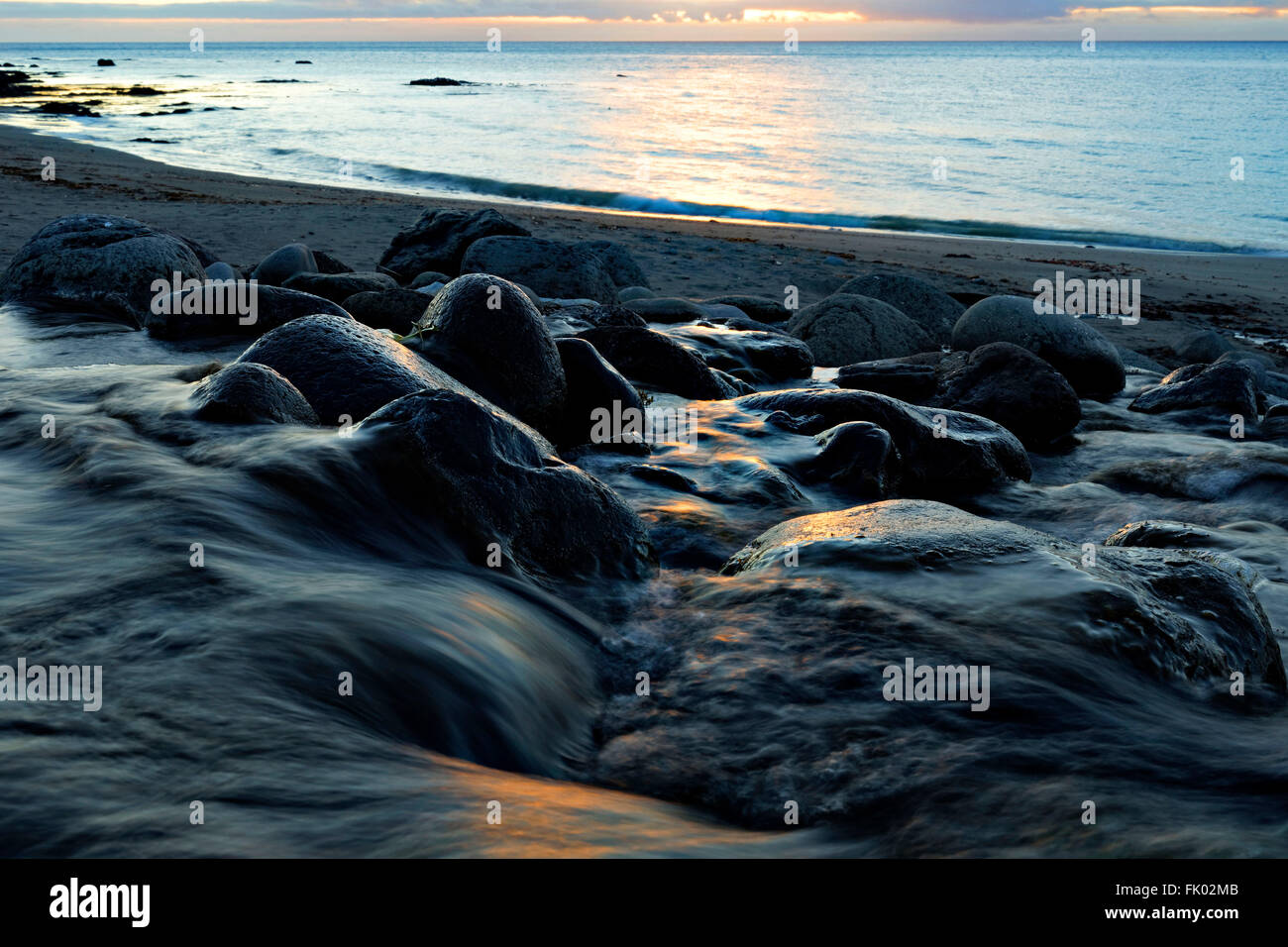 Acqua di ruscello che scorre su pietre sulla spiaggia al tramonto, Reykjanes, Westfjords, Islanda, l'Europa. Foto Stock