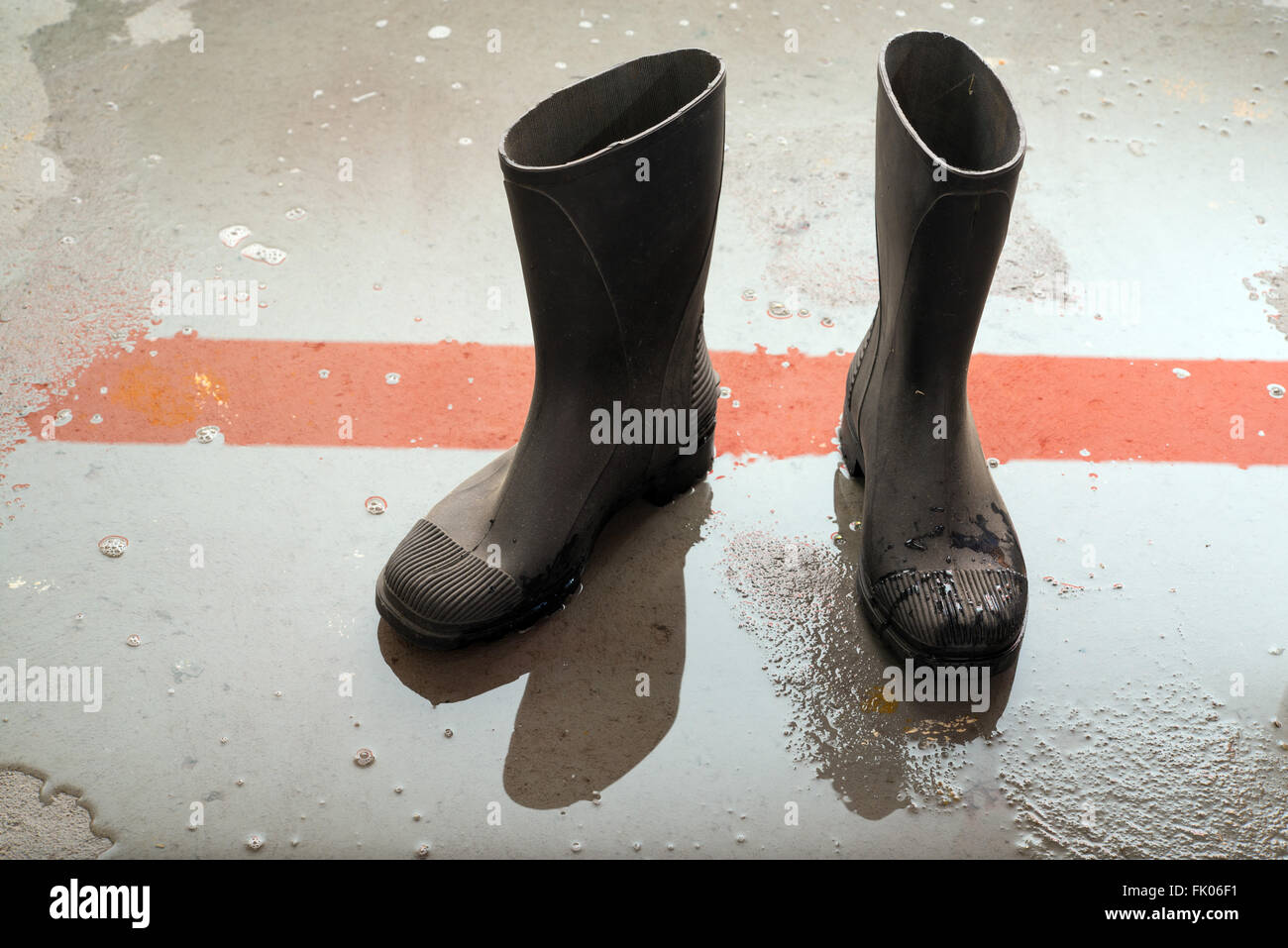 Stivali di gomma su un umido pavimento di cemento Foto Stock