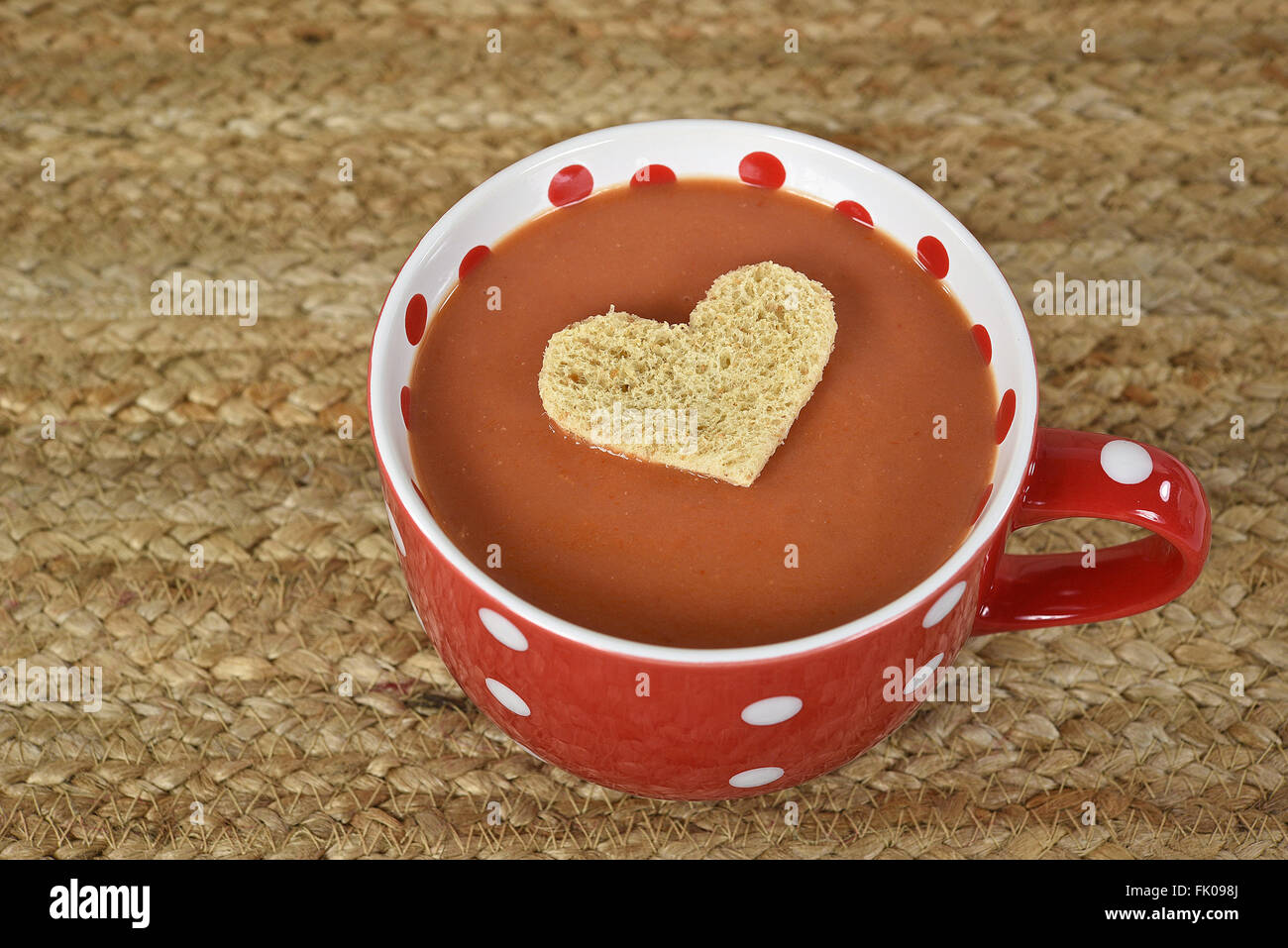 Pane unico cuore galleggiante nella minestra di pomodoro in rosso e bianco polka dot zuppa mug. Foto Stock