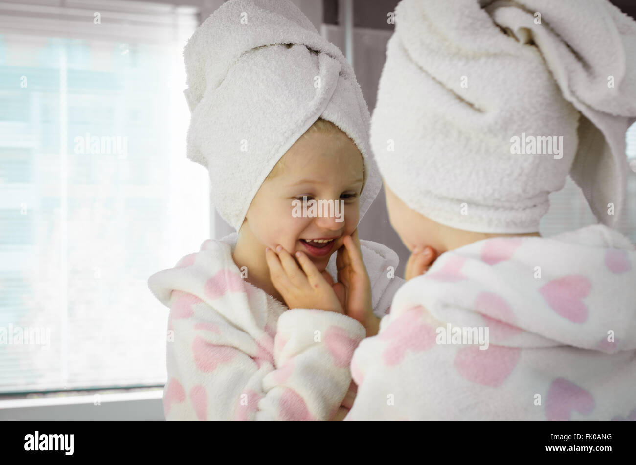 Bella ragazza in accappatoio a sorridere a se stessa nello specchio Foto Stock