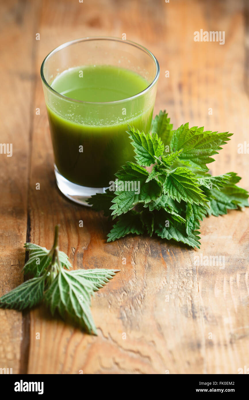 Ortica foglie e bicchiere di fresco succo di ortica, su un tavolo di legno. Foto Stock