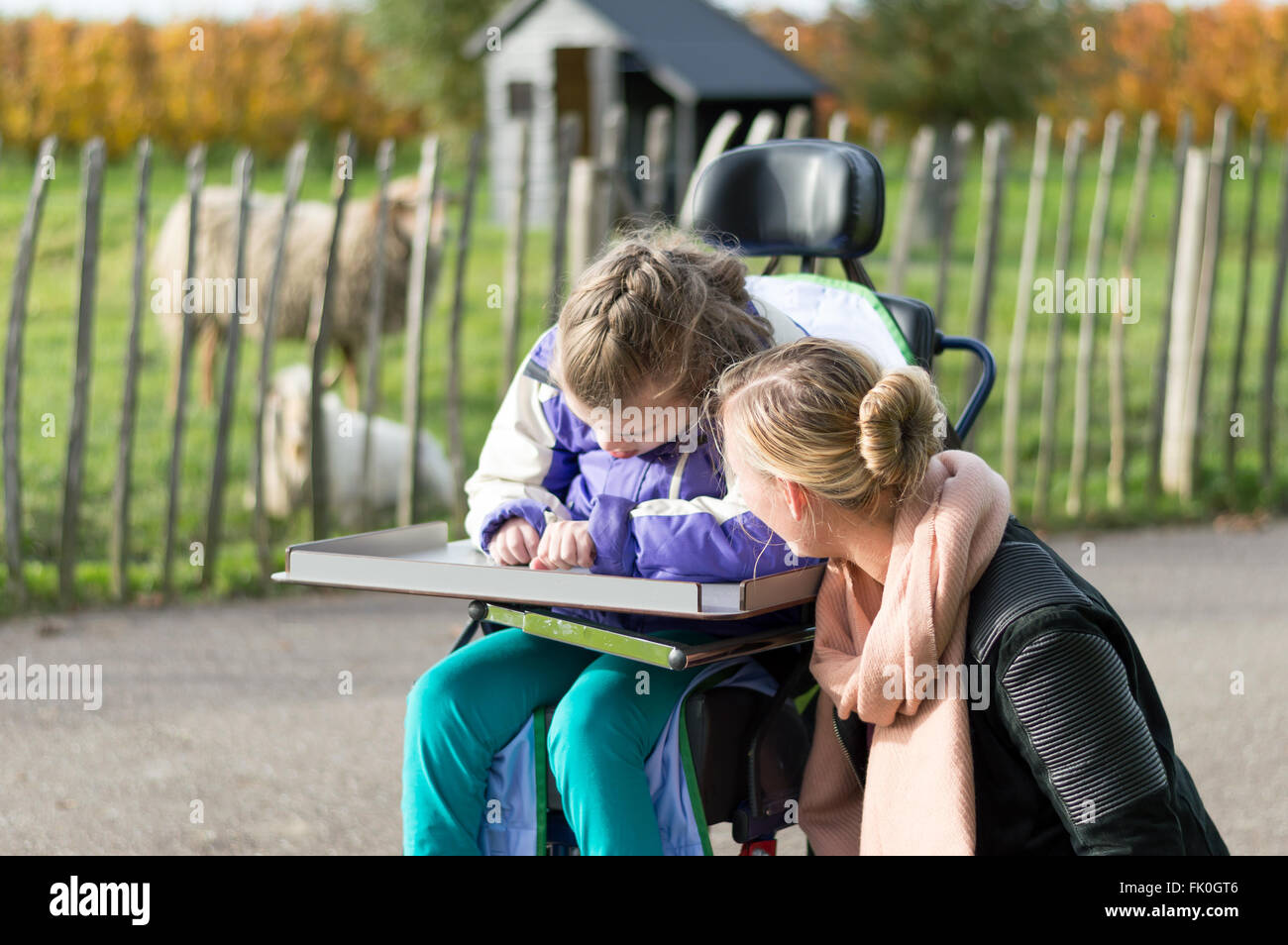 Un bambino disabile su sedia a rotelle rilassante al di fuori di un volontario lavoratore di cura Foto Stock
