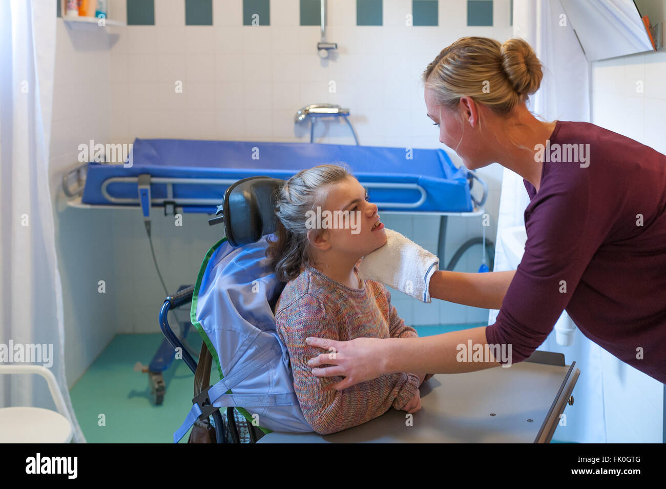 Un bambino disabile su sedia a rotelle essendo curata da un volontario lavoratore di cura Foto Stock