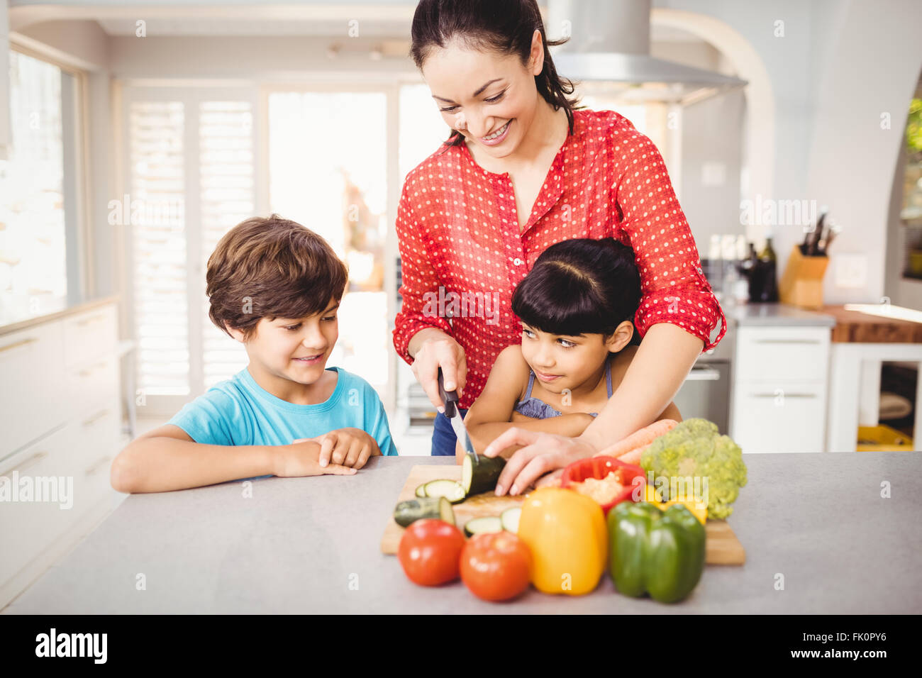 Donna tritare verdure mentre i bambini in piedi dalla tabella Foto Stock