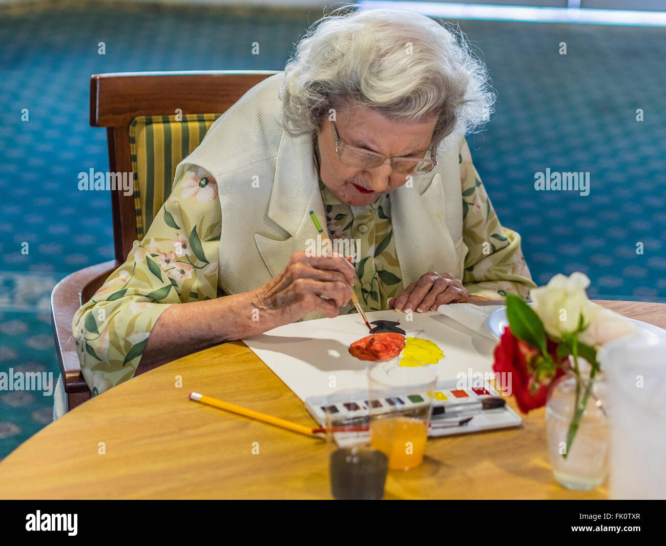 Una femmina senior citizen vernici in un acquerello di classe per gli anziani al Garden Court senior residence a Santa Barbara, California. Foto Stock