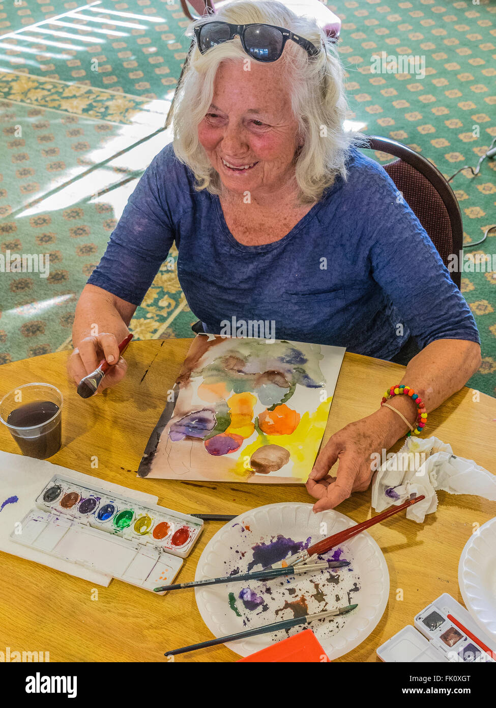 Una femmina senior citizen vernici in un acquerello di classe per gli anziani al Garden Court senior residence a Santa Barbara, California. Foto Stock