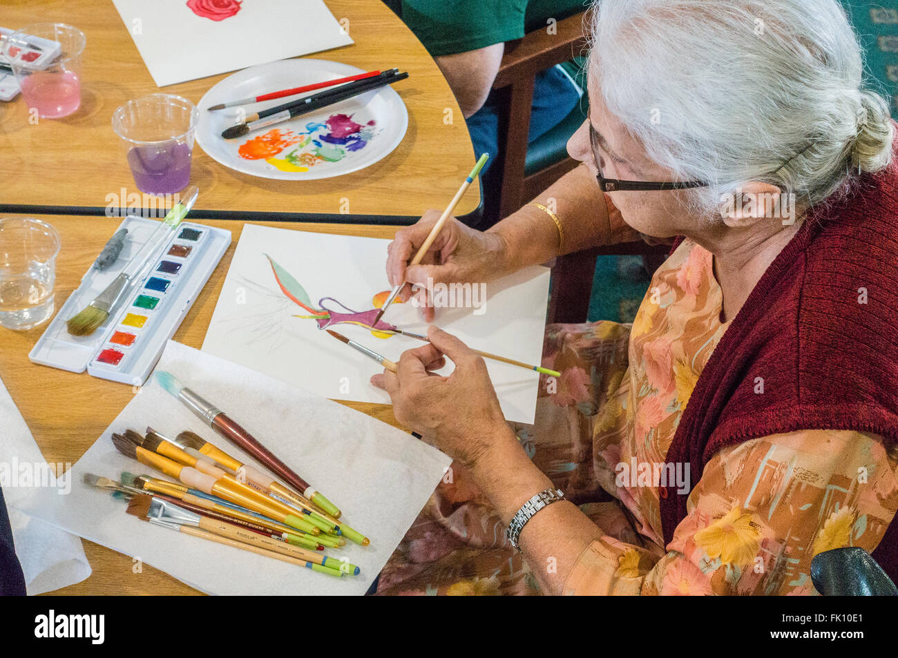 Una femmina senior citizen vernici in un acquerello di classe per gli anziani al Garden Court senior residence a Santa Barbara, California. Foto Stock