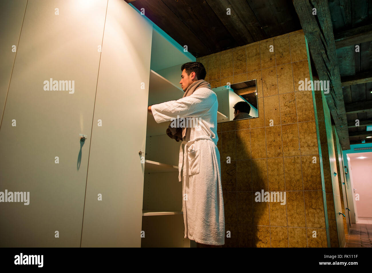 Bel giovane indossare accappatoio bianco, in piedi nel bagno termale accanto a ripostiglio Foto Stock