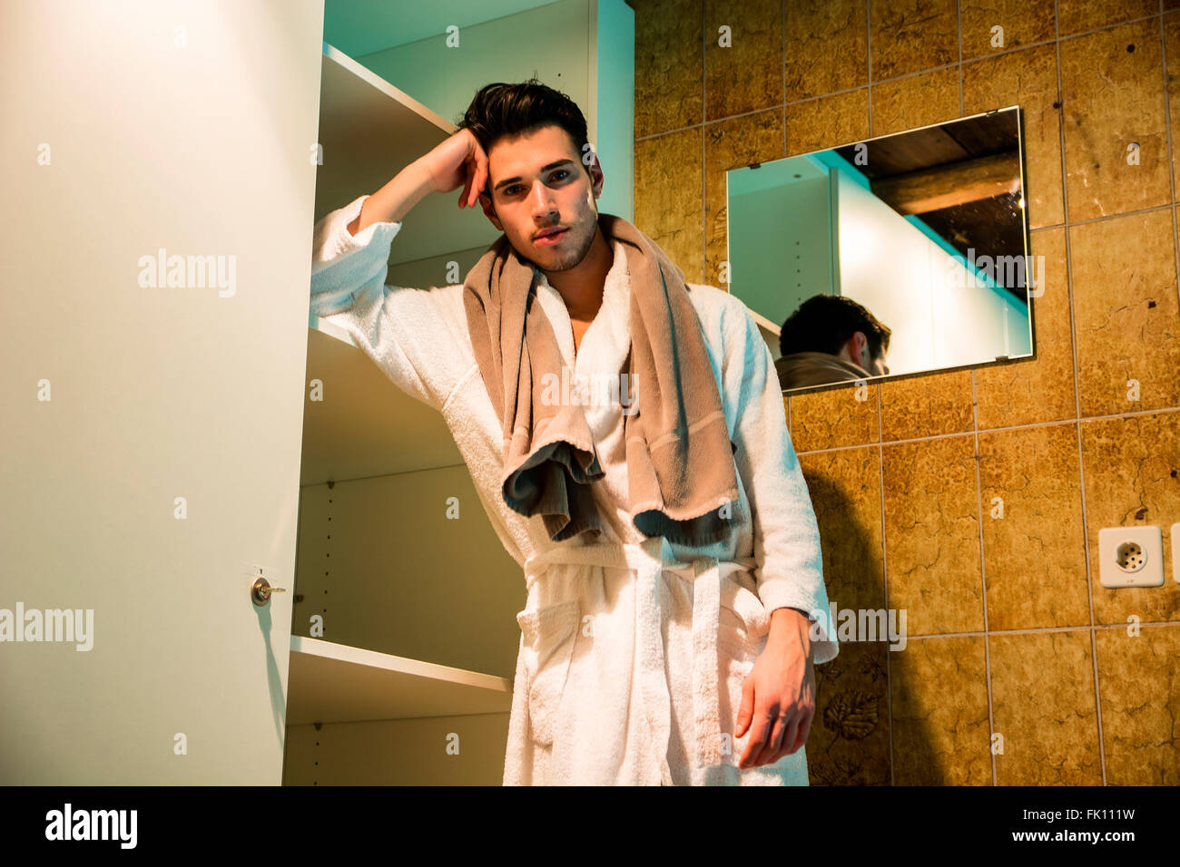 Bel giovane indossare accappatoio bianco, in piedi nel bagno termale accanto a ripostiglio Foto Stock