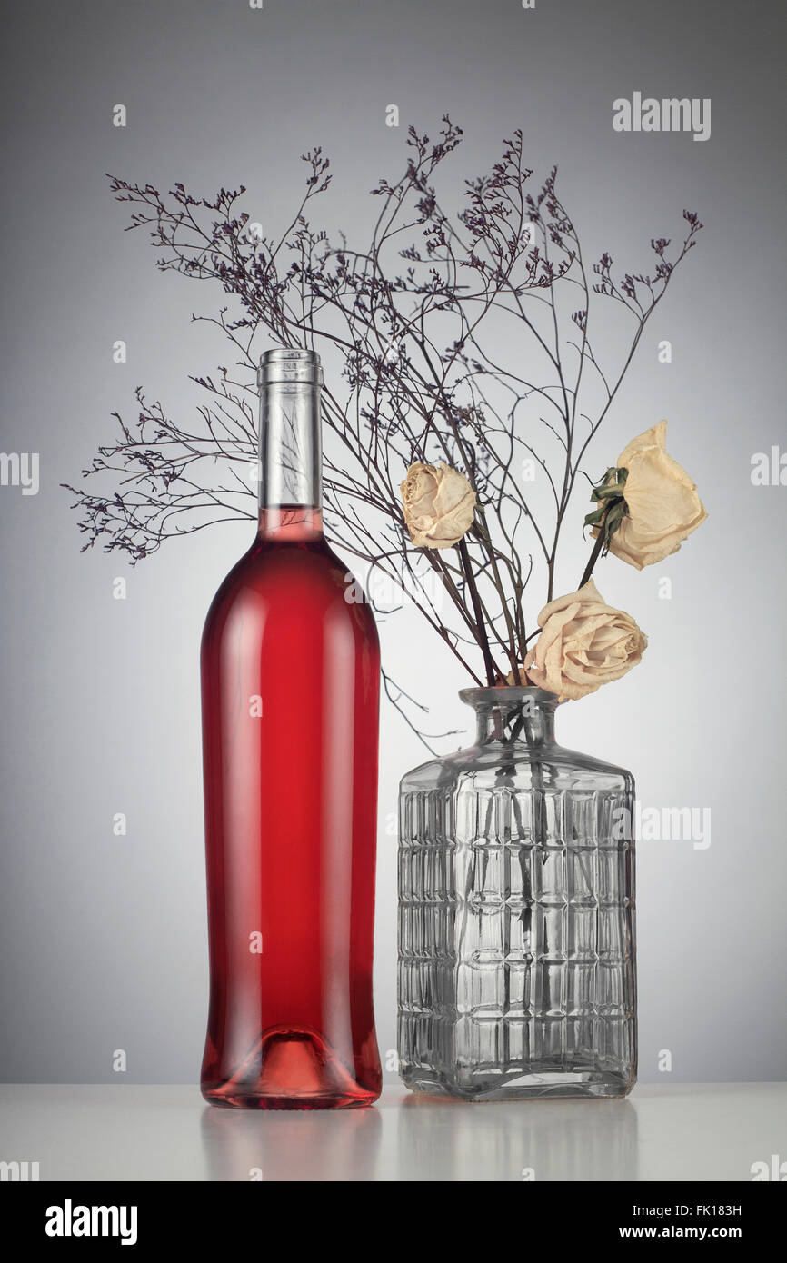 Vino rosato bottiglia con nessuna etichetta accanto a appassiti rose bianche in un vaso Foto Stock