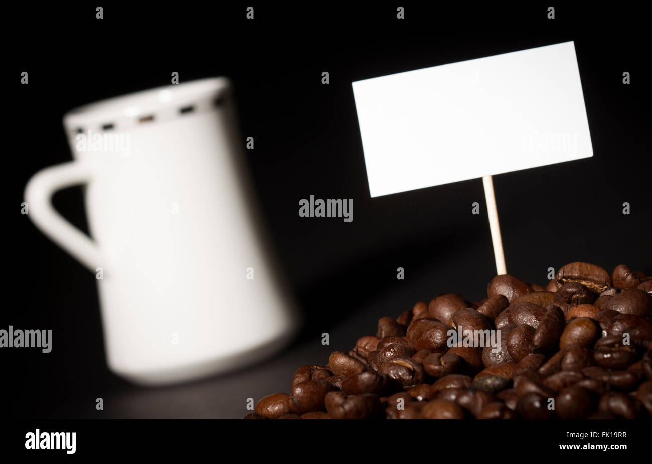 Un mucchio di chicchi di caffè con un segno vuoto al di sopra di esse e un bianco tazza da caffè in background Foto Stock