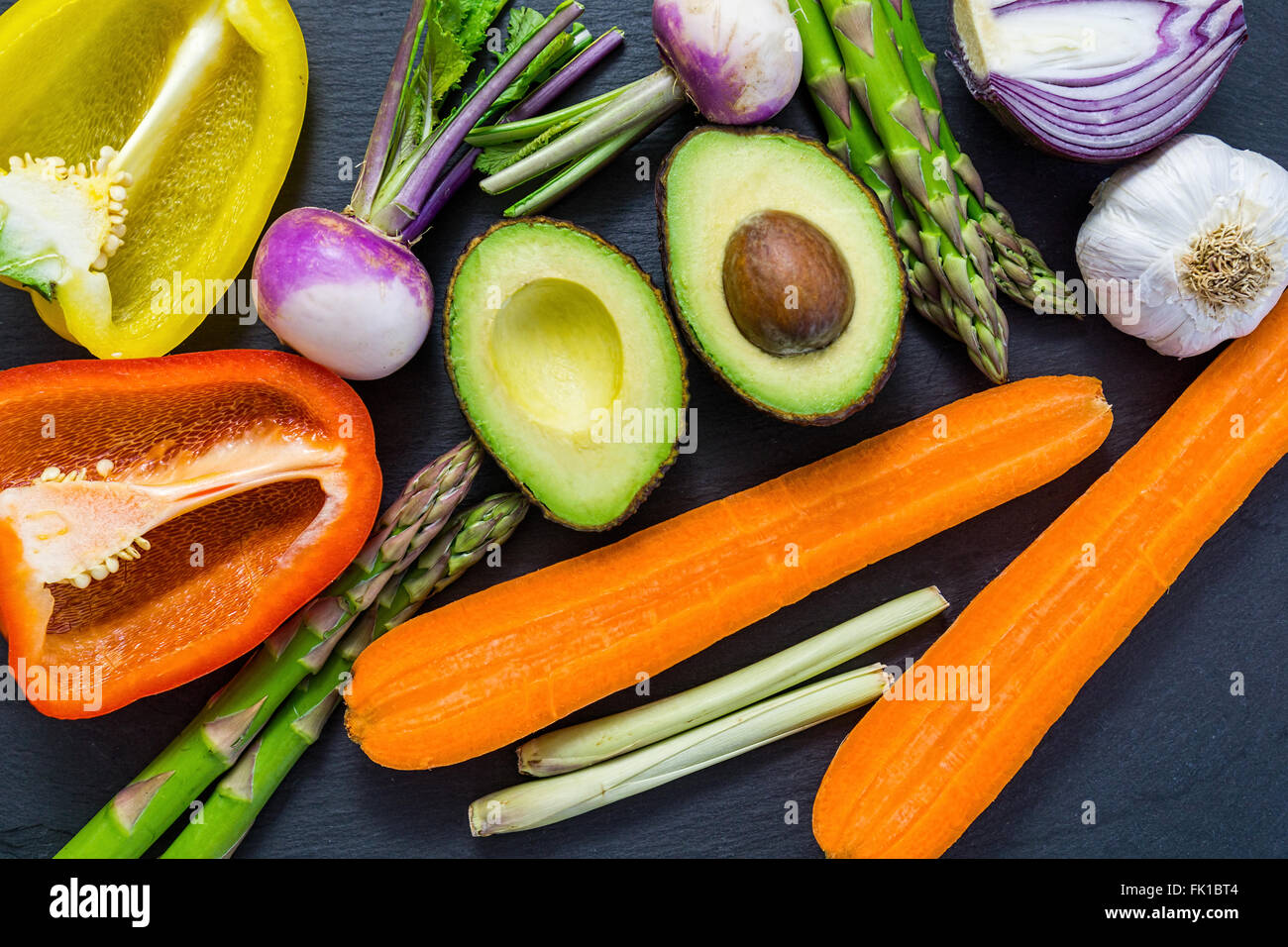 Fette di verdure fresche al buio su un bordo, vista dall'alto, pianamente, avocado, peperoni, cipolla Foto Stock