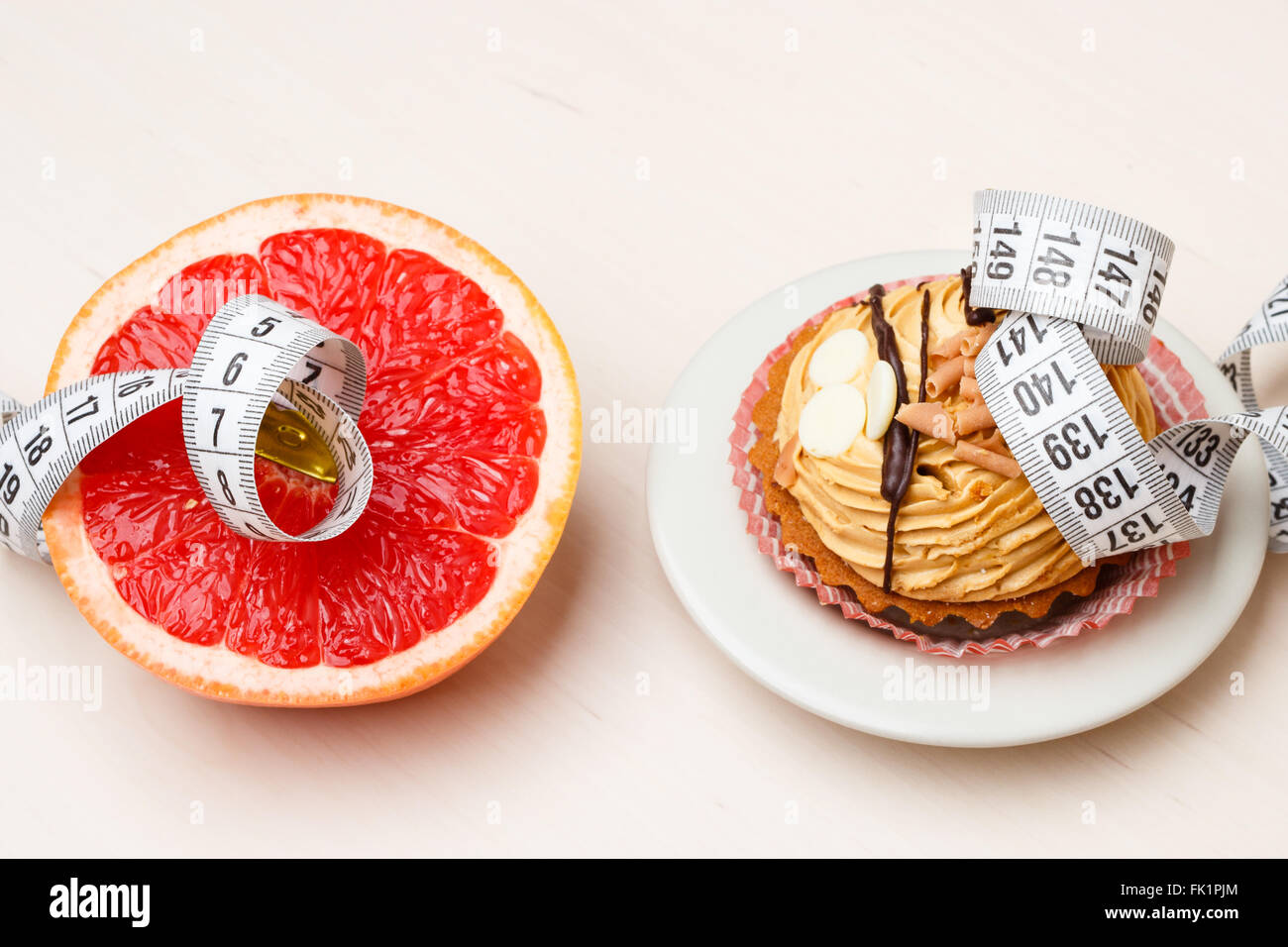 Concetto di scelta: sano a basso contenuto calorico o malsana alto-caloria cibo, dimagrimento o ingrasso. Pompelmo e torta cupcake con nastro di misurazione Foto Stock