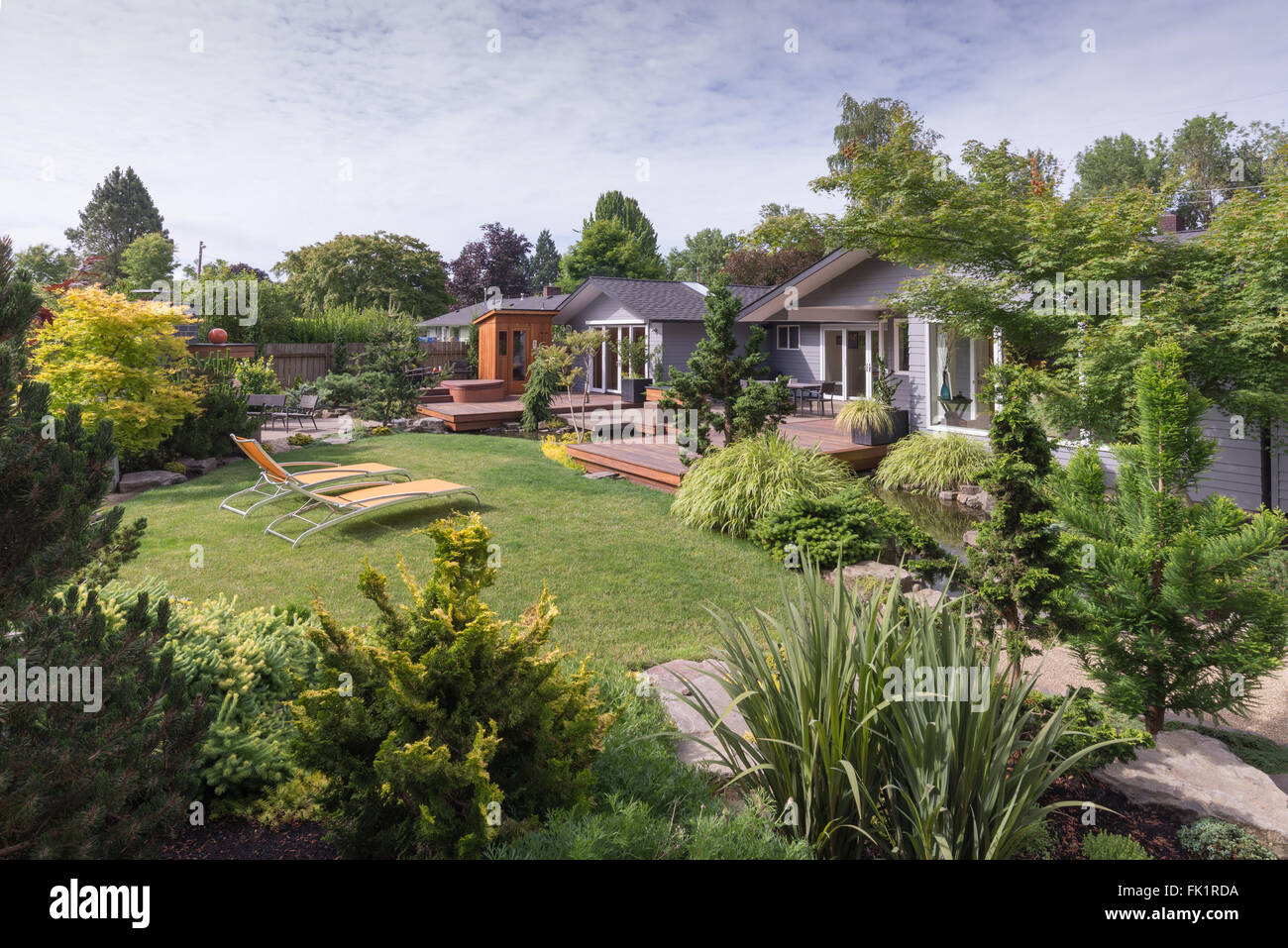 Una casa contemporanea può essere visto al di là del backyard prato con rock e paesaggio sempreverde in primo piano su un clima estivo Foto Stock