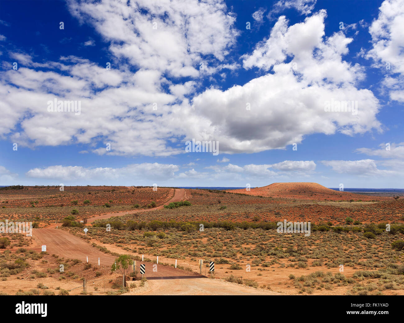 Piano terreno rosso outback plain vicino Flinders Ranges National Park con strada sterrata e solitaria lontana colle sotto il cielo blu Foto Stock
