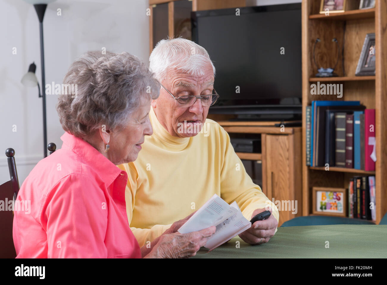 Una coppia di anziani nella loro casa confortevole a lavorare insieme come si leggono le istruzioni per il loro nuovo telefono. Foto Stock