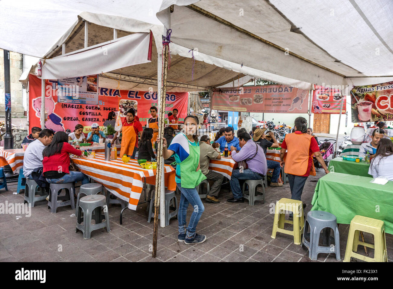 Piuttosto giovani server nel grembiule verde si prende una pausa come pranzo folla si assottiglia in food court Llano mercato del venerdì, Oaxaca Foto Stock