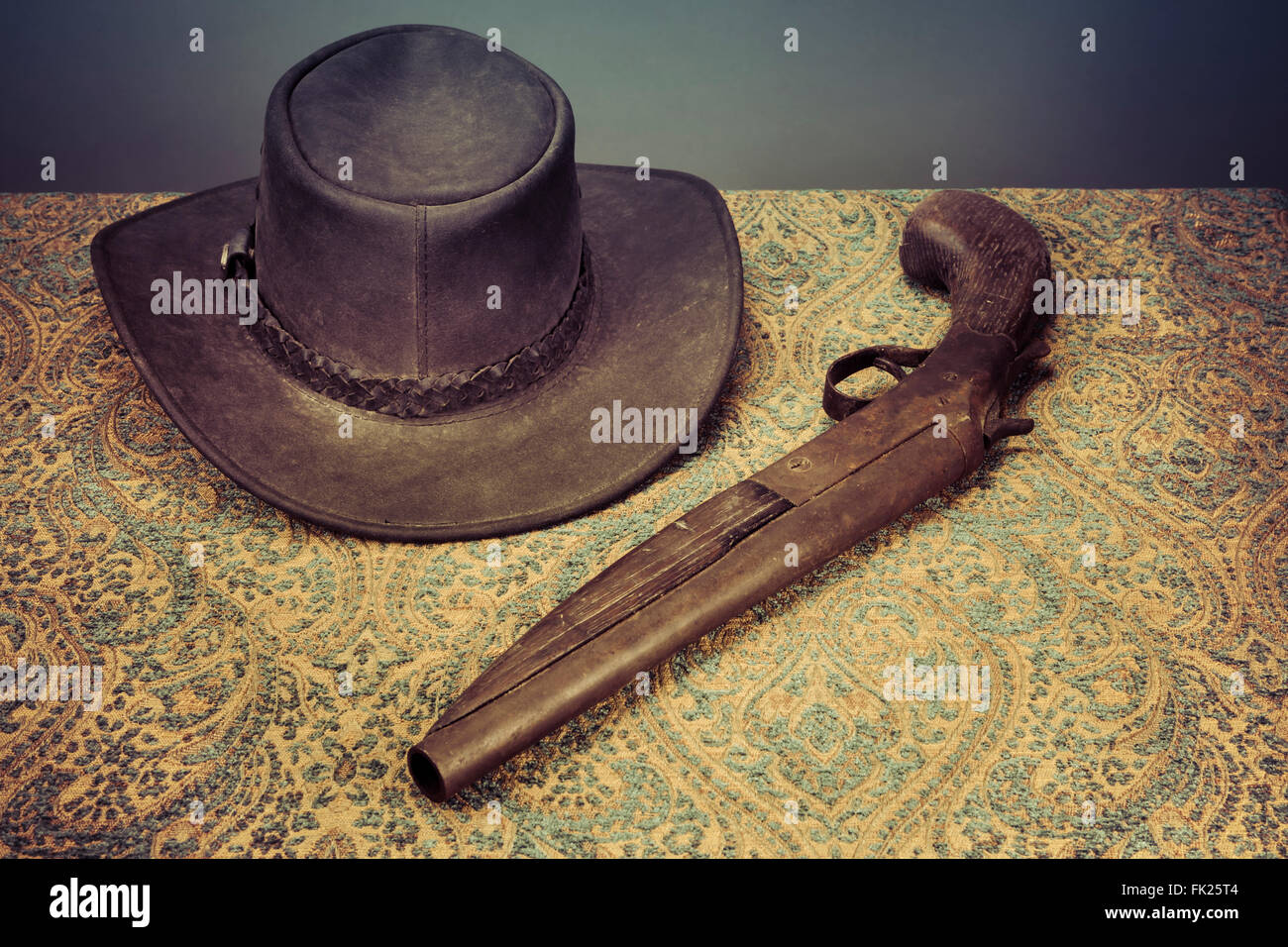 Antique Cappello in cuoio e una pistola su un tavolo vintage panno con colorazione retrò. Foto Stock