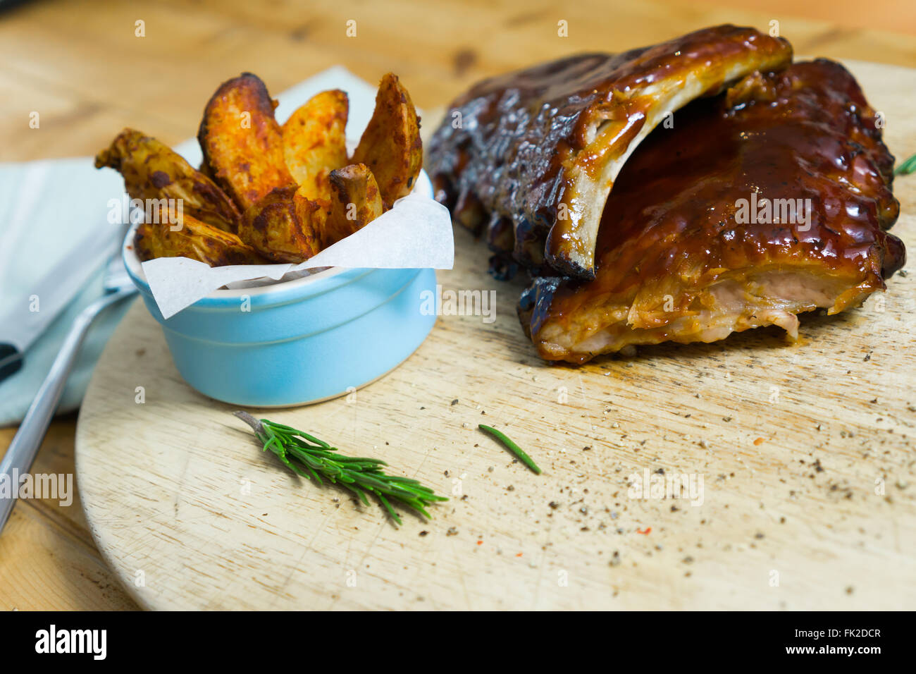 Smoky barbecue nervature con spicchi di patate erbe e spezie, su un vassoio in legno Foto Stock