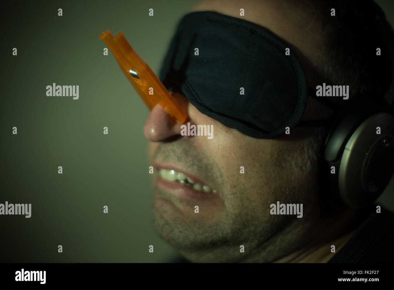 Un uomo che indossa una molletta da bucato sul suo naso, cuffie e una mascherina per gli occhi Foto Stock
