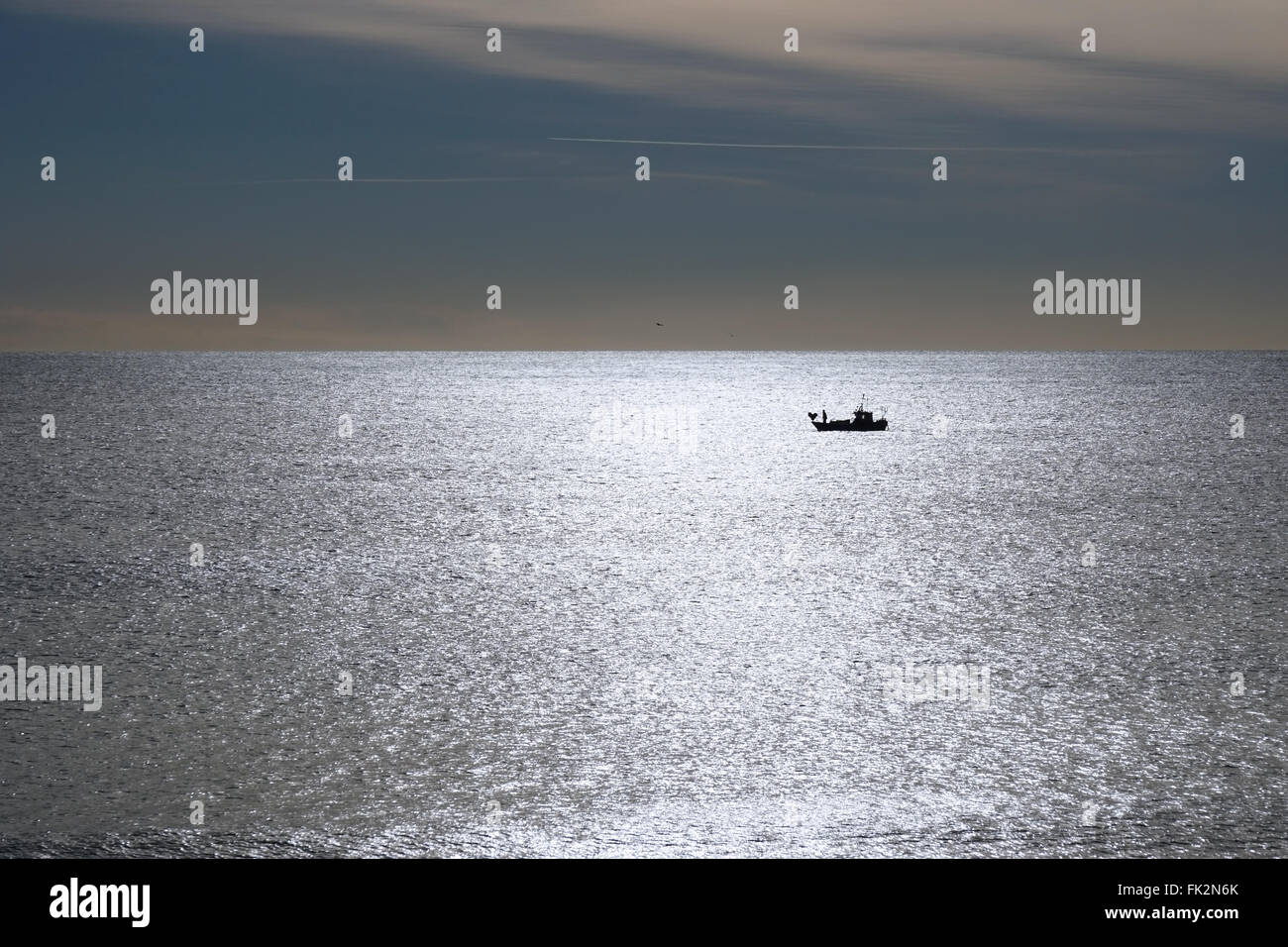 Pescatore solitario retroilluminato in barca come silhouette sul mare calmo Foto Stock