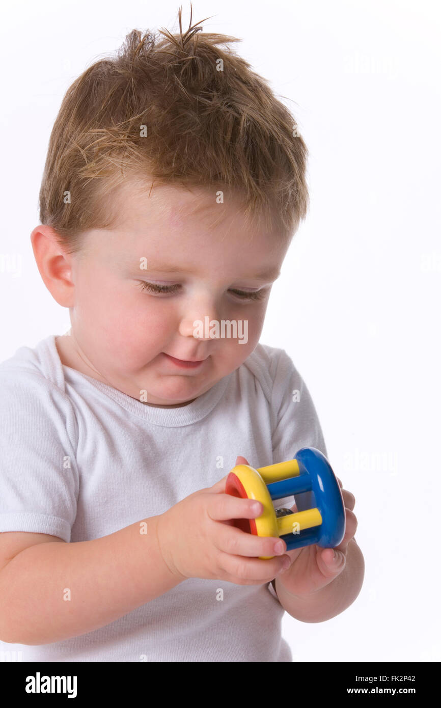 Poco Toddler Boy è guardando al suo giocattolo in sua mano su sfondo bianco Foto Stock