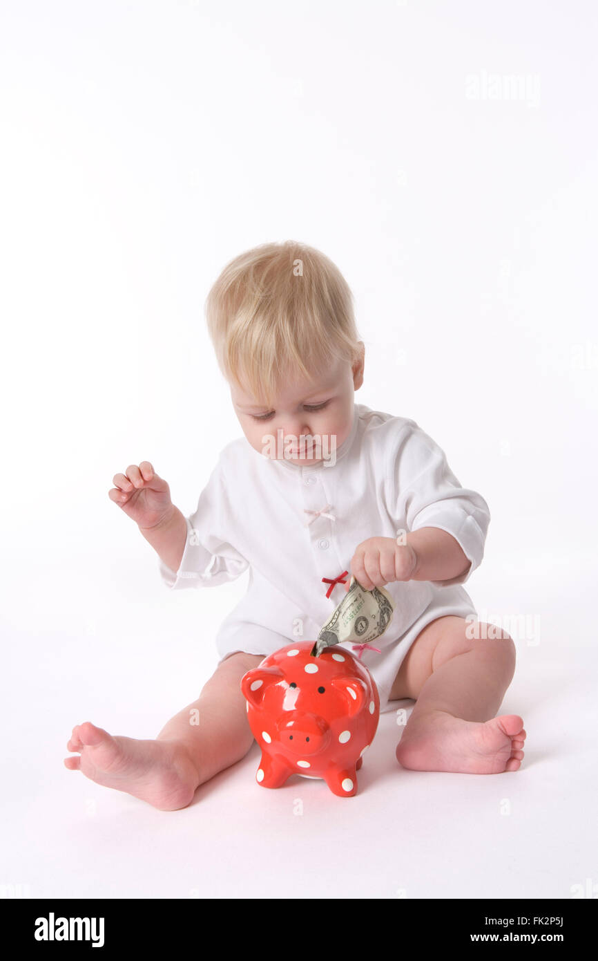 Baby girl sta mettendo un dollaro in un Piggy-bank su sfondo bianco Foto Stock