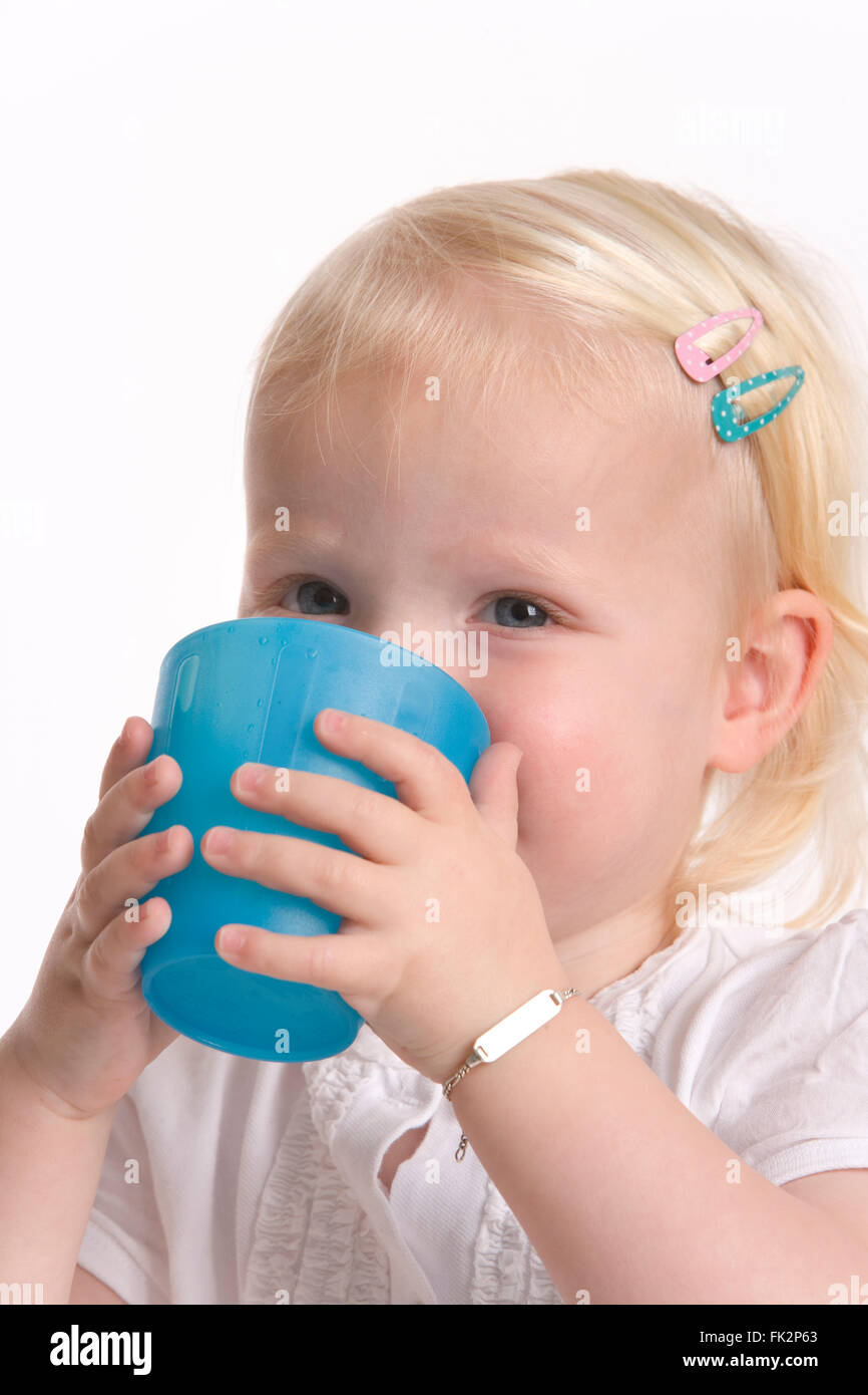 Il Toddler ragazza è di bere da un blu tazza in plastica su sfondo bianco Foto Stock
