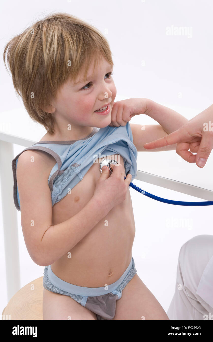 Little Boy è in ascolto per il suo ritmo cardiaco con uno stetoscopio su sfondo bianco Foto Stock