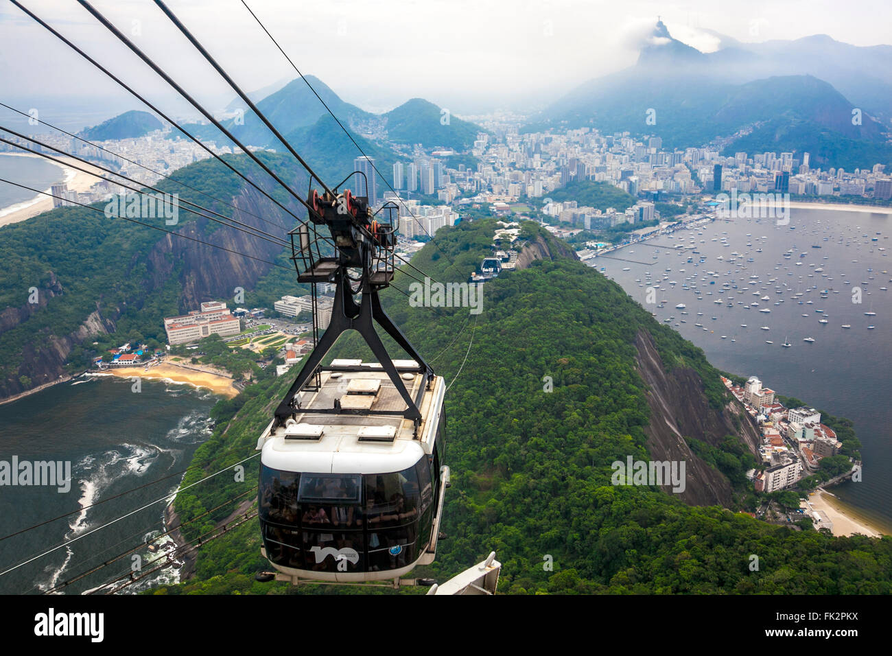 Un cavo carrello scendendo Sugarloaf Mountain (Pão de Açúcar) a Rio de Janeiro in Brasile con Cristo il Redentore statura davanti Foto Stock
